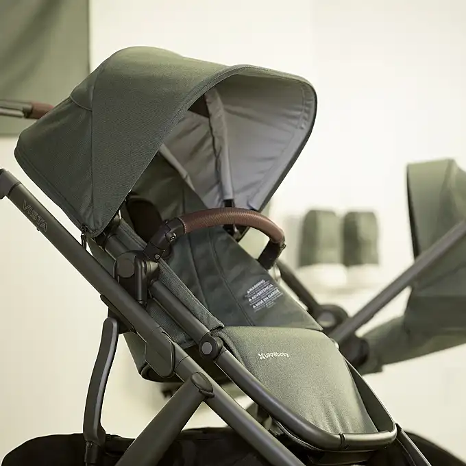 Close-up of a UPPAbaby Vista stroller in green fabric with a leather handlebar, extended canopy, and visible seat details.
